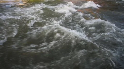 Close up of a rushing river with a slow pan up to reveal a foot bridge in mo Stock Footage 243456217
