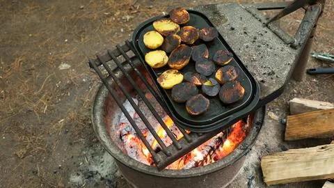 A close-up of rustic potatoes cooking on a campfire grill grate, highlighting Stock Photos