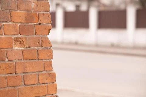Close up of rustic red brick wall edge with blurred street and white fence .. Stockfoto's