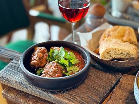 Close up of a rustic wooden table with black bowl of braised meat in tomato Stock Photos