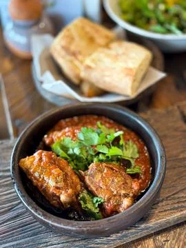 Close up of rustic wooden table with black bowl of braised meat in tomato sauce Foto stock