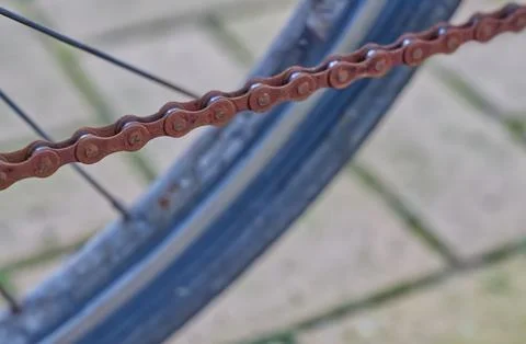 Close-up of a rusty bicycle chain and wheel on a blurred pavement background. Stock Photos