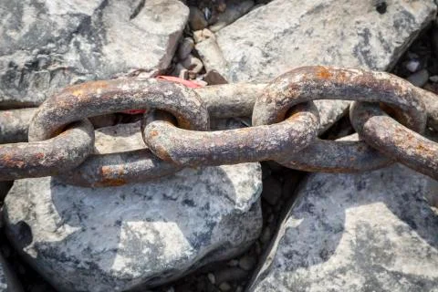 Close up of a rusty big old chain laying on rocks Stock Photos
