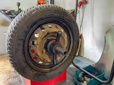 Close-up of a rusty car wheel fixed on a balancing machine in a garage. Techn Фото