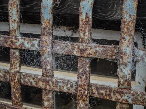 Close up of rusty iron window security bars covered in cobwebs Stock Photos