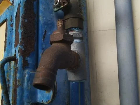 Close-up of a rusty metal pipe with an elbow joint, attached to a blue, wea.. Stock Photos