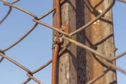 Close-up on a rusty metal pole rusty steel mesh chain link.An old fence. Stock Photos
