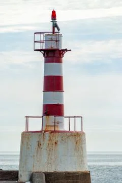 Close up of a rusty old red and white striped harbor lighthouse at the end of Stock Photos