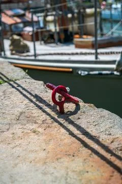 Close up of a rusty red mooring cleat fastened to a stone quay with a boat Foto stock