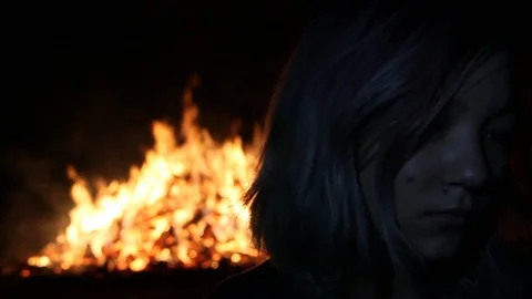 Close up on sad looking girl as fire burns behind her Stock Footage 122803115