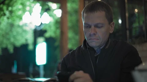 Close-up of a Sad Man Looking at a Smartphone Sitting in a Night Cafe Stock Footage 97662247