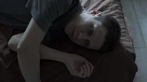 Close-up of sad man lost in thought. Man lying on bed, overwhelmed by depression 스톡 동영상 309908259