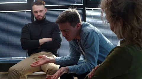 Close-up of sad smiling young man sharing problem sitting in circle during group Stock Footage 154890782