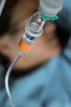 Close up saline solution drip with a patient lying on a bed on the background Stock Photos