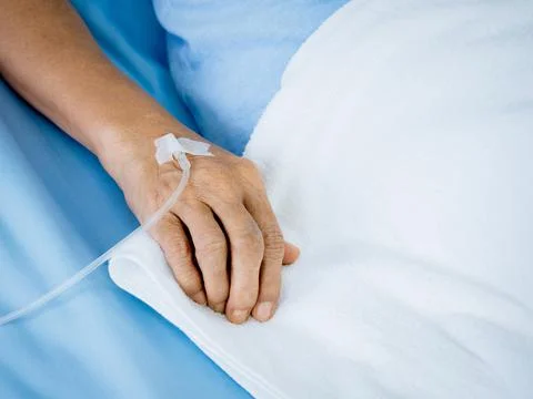 Close up saline solution in senior patients hand in blue gown lying on the be Stock Photos