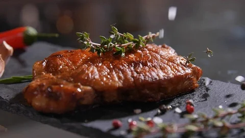 Close-up of salt and pepper falling on the freshly-cooked grilled meat on stone Stock Footage 107435769