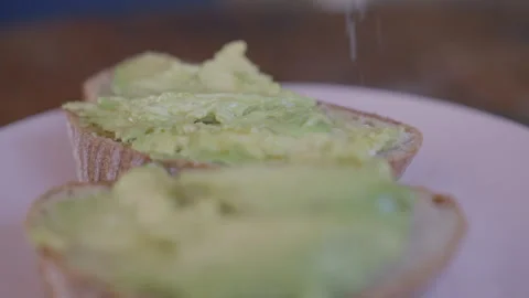 Close-Up of salt falling on a toast with fresh mashed avocado Stock Footage 255030617