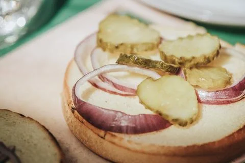 Close-up of sandwich preparation featuring sliced pickles and red onions on.. Stock Photos