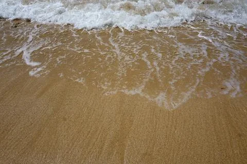Close-up of sandy beach with gentle waves lapping shore Stock Photos