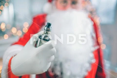 Close up of Santa Claus stands and holds vape in hand. He shows it on camera. Stock Photos