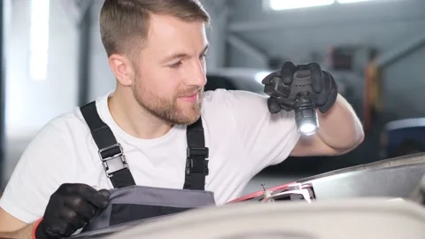 Close-up of satisfied attractive auto mechanic inspecting car with flashlight Stock-Footage 212344852