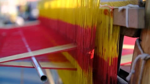 Close-up scene in which a saree is being woven from red and yellow silky Stock Footage 243888936