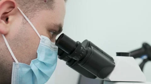 Close-up of a scientist examining samples under a microscope Видео 269299359