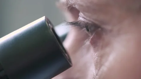 Close-up of a scientist looking through a microscope in a lab. Vídeo Stock 253334819