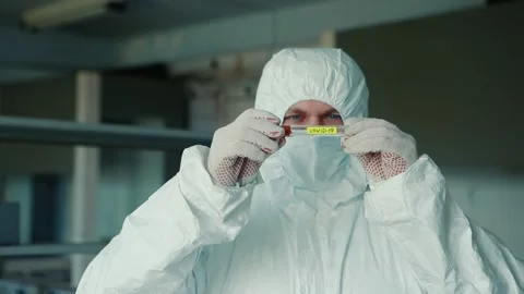 Close-up of a scientist in a mask and protective suit holds and examines a Stock Footage 131439168