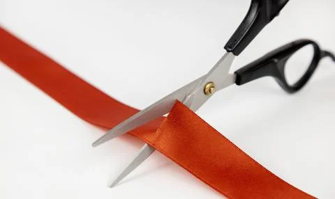 Close-up of scissors cutting a red satin ribbon. Stock Photos