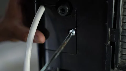 Close-up of a screwdriver removing a screw from a black appliance beside a .. Видео 338319446