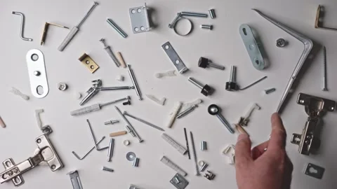 Close-up of screws, dowels, and hinges on a white table, hands organizing p.. Video stock 293461916