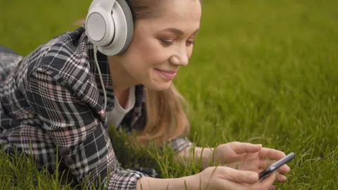 Close-up, scrolling, searching the Internet, a young woman lies on the grass in Stock Footage 127545202