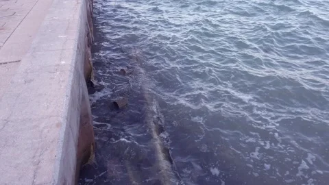 Close up of sea wall on the left and blue water , Small waves crashing up agains Stock Footage 262371152