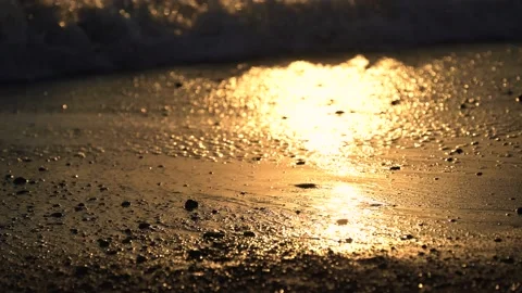 Close-up of sea waves reflecting sunset sunlight hitting sandy beach Stock Footage 133376483
