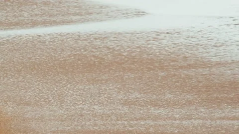 Close-up of sea waves running on a sandy beach. White sea foam bubbles on the Stock Footage 185552408