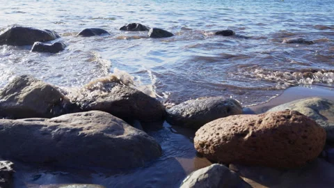 Close-up of sea waves splashing over smooth rocks on a sandy beach Stock Footage 327713007