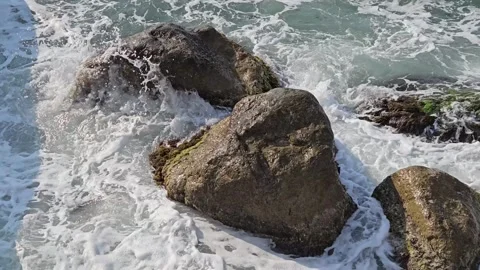 Close-up of sea waves with white foam splashing over large coastal rocks. Stock Footage 317578807