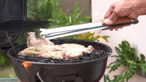 Close-up of seasoned meat being placed on a charcoal BBQ grill with tongs and Stock Footage 337895149