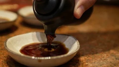 Close up selective focus to a ceramic plate while pouring shoyu soy sauce f.. Video stock 254047885