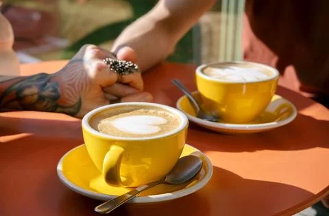 Close up selective focus coffee cups with hearts and hands of man and woman.. Stock Photos