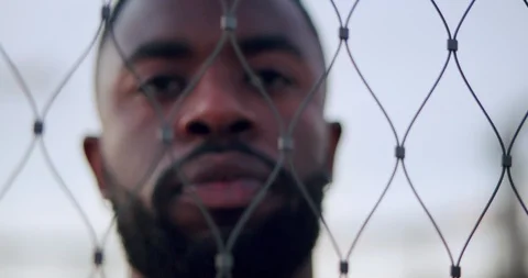 Close up of self-confident Afro-American man looking through metal net outdoor Stock Footage 123665013