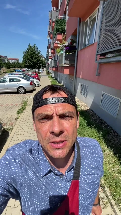 Close-up selfie of man walking along urban apartment sidewalk under bright Видео 344583880