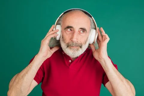 Close-up senior grey-haired man in headphones isolated over green background. Stock Photos