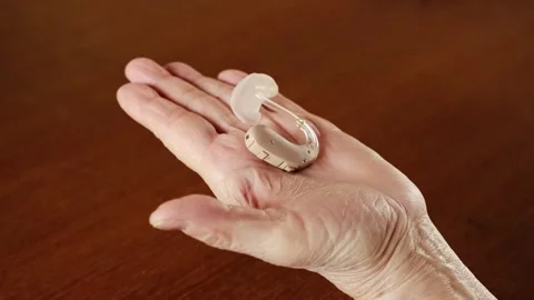 Close-up of a senior hand gently holding a modern hearing aid device over a hand Stock Footage 310232859
