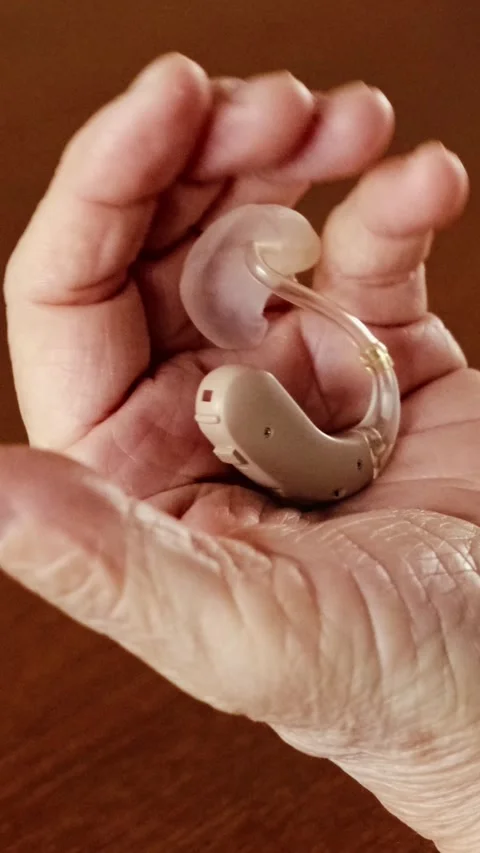 Close-up of a senior womans hand gently holding a beige hearing aid, symbol.. 動画素材 310607668
