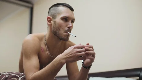 Close up serious topless good-looking fit young man smoking cigarette in bed at Stock Footage 121065115
