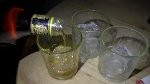 Close-up serving whiskey in glasses with ice at night on a wooden table in 4K Stock Footage 155792323