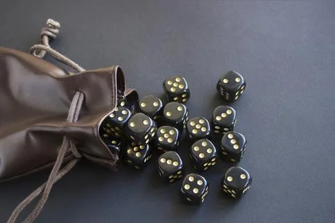 Close-up set of gaming dice rolled out of leather bag on dark background. Con Stock Photos