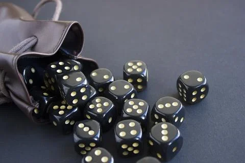 Close-up set of gaming dice rolled out of leather bag on dark background. Con Stock Photos